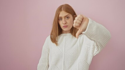 Sticker - Angry redhead woman in sweater, showing thumbs down with negative gesture over pink background