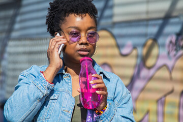 Wall Mural - urban black woman talking on the phone and drinking a soft drink on the street