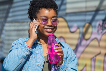 Wall Mural - urban black woman talking on the phone and drinking a soft drink on the street