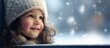 A smiling little girl in a white T shirt sits on a windowsill looking out the window on a snowy winter day The image captures the essence of children childhood and emotions with copy space provided