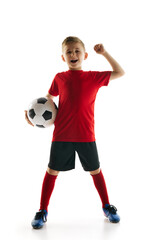 Victory. Goal. Young boy as soccer player in sportwear clenched fist holds football ball against white studio background. Concept of professional sport, championship, youth league, hobby. Ad