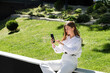 © MM - A woman in a park in a white shirt and white pants looks at the phone