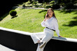 © MM - A woman in a park wearing a white shirt and white pants speaks on the phone.