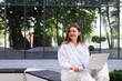 © MM - A woman in a park in a white shirt and white pants sits with a laptop in her hands near the office