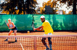 Couple playing recreational tennis on a clay court during the day.