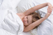 Kid waking up and stretching, raised hands. Portrait of little child lying on big bed. Concept of happy children having good time at home. Child awaked up in bed.