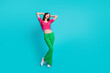 Full size photo of adorable gorgeous girl wear pink knit top green trousers hold arms behind head isolated on blue color background