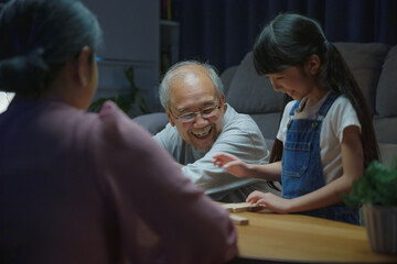 Happy grandparents Asian family enjoy playing toy block with little daughter together in home living room at night time, Smiling parent having fun play build constructor tower of wooden blocks