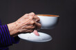 Close-up of a senior woman's hand holding a white coffee cup while standing on a gray background.