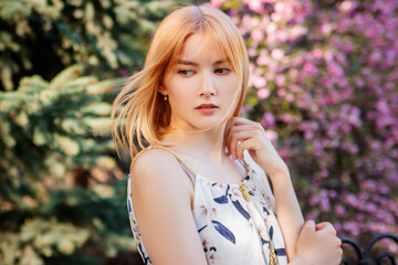 Portrait of a young attractive woman posing against the background of blooming sakura flowers.