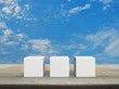 Three white block cubes on wooden table over blue sky with white clouds