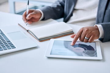 Fototapete - Tablet, book and hands of businessman in office with finance graphs, charts or data online. Laptop, career and male financial advisor working with digital technology and writing notes for budget plan