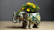 A ceramic elephant planter with yellow flowers sits on a wooden surface against a grey background.