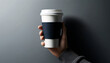 A person's hand holding a disposable coffee cup against a plain gray background