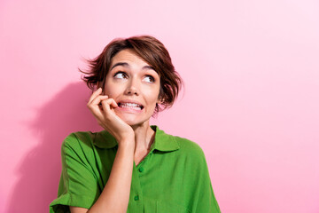 Wall Mural - Photo of scared unsure young lady wear green shirt biting fingers looking empty space isolated pink color background