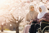 Fototapeta  - Young arabic disabled teenager girl woman in hijab sitting in wheelchair walking in spring blossom park fresh air together with caregiver, mother or grandmother Health and care for disability children