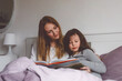 Loving mother and school kid girl reading book together. Happy family, woman and cute daughter together in bed. Family care, evening routing and lifestyle.
