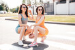 Two young beautiful female in trendy summer cycling shorts, top clothes. Sexy carefree women posing in street at sunny day. Positive models having fun. Cheerful and happy. In sunglasses