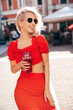 Young beautiful smiling hipster woman in trendy summer clothes. Carefree model posing in the street. Holding and drinking fresh vegetable cocktail smoothie drink in plastic cup with straw