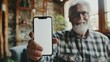 © Alina Zavhorodnii - An old, elderly man is holding a modern smartphone with the screen facing forward and smiling. Mockup