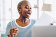 Overjoyed african american hipster girl excited with good news reading from paper sitting near laptop computer,emotional dark skinned woman with funny face celebrating victory of online project