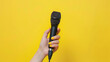 Female hand holding microphone on yellow background