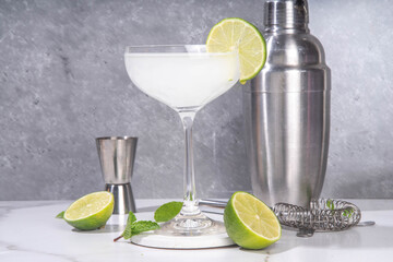 Wall Mural - Gimlet citrus alcohol cocktail. Sweet and sour boozy alcoholic drink, with gin or vodka and lime garnish, on light grey with hard light and bar utensils