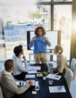 © peopleimages.com - Black woman, coach and discussion with team in meeting, presentation or conference on project at office. Female person or speaker talking to employees with paperwork, documents or ideas at workplace