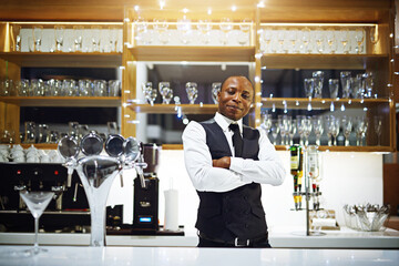 Black man, bartender and confident portrait in hotel, hospitality and counter server for alcohol. Male person, cocktail and martini at winery or restaurant, waiter pride and barman arms crossed