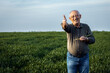 Portrait of smiling senior farmer standing in wheat field showing thumb up.