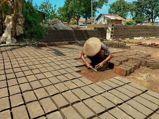 Selective focus. A male worker is making red bricks (batu bata merah) using a wet clay field using a rectangular box shaped mold and then dried and burned in the sun. Indonesia.