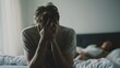 © Oulaphone - Depressed man sitting and covering his face on bed while having problems with girlfriend.