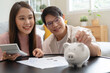 Happy asian family young couple love hand holding piggy bank to save and model house for saving money wealth to buy real estate for new home. Financial planning, business finance concept. Housing loan
