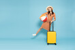 Happy young Asian woman traveler with luggage and holding beach ball isolated on sky blue background, Tourist girl having cheerful holiday trip concept, Full body composition