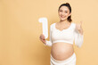 Portrait of Happy Asian pregnant woman standing and holding 1 number or one isolated on brown background