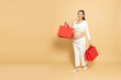 Happy Asian pregnant woman holding red shopping bags isolated on brown background, Motherhood and Pregnancy Concept, Full body composition