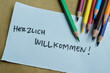 Concept of Herzlich Willkommen write on sticky notes isolated on Wooden Table.