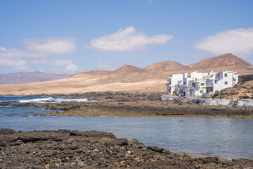 Wall Mural - Bay and typical houses of the fishing village of Caleta de Caballo. White houses. Rock coast in the foreground. Turquoise water. Calm sea. Caleta de Caballo, Lanzarote, Canary Islands, Spain