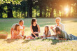© Soloviova Liudmyla - Big family sitting on the picnic blanket in city park during weekend Sunday sunny day. They are smiling, laughing and eating boiled corn and watermelon. Family values and outdoors activities concept.