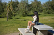 Young, beautiful, brunette woman wearing a white sweater, denim miniskirt and sunglasses, taking pictures with her smartphone sitting on a park bench on a sunny day. Beauty, fashion, trend concept.