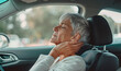 Portrait of elderly gray-haired woman massaging her hindhead while she felt neck ache. Female sitting on co-driver car seat. Medicine, health care, spinal column and Osteochondrosis issues concept.