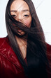 Stylish woman with long black hair in red leather jacket feeling the breeze and looking confident