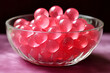 A glass bowl on a table filled with pink chewing jelly candies in sphere round shape closeup shot. Sweet snack dessert