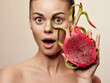 Woman fascinated by exotic dragon fruit, holding it in front of her face with eyes wide open