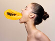 Woman eating papaya fruit with mouth wide open and holding in hand, close up view
