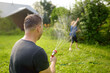 © Maria Sbytova - Funny little boy with his father playing with garden hose in sunny backyard. Preschooler child having fun with spray of water. Summer outdoors activity for kids.