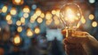 © VISUAL BACKGROUND - Person holds light bulb against blurred background, person holds light bulb in their hand.