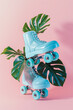 Minimal creative concept with flying retro blue roller skates and tropical leaves against pink pastel background.