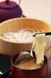 A bowl of Udon noodles with a pair of chopsticks, accompanied by a small bowl of soup