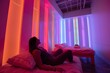 A woman laying on a bed in a room illuminated by vibrant color-changing lights, A calming, color-changing LED lighting system to promote healing and relaxation